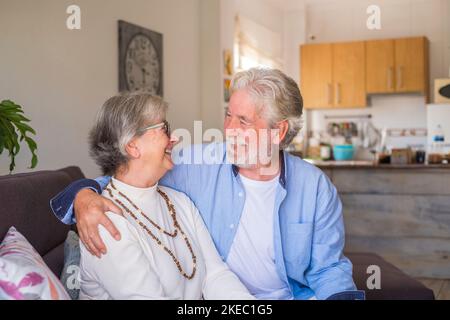 Portrait de couple de personnes âgées riant et s'amusant ensemble assis sur le canapé de la maison à l'intérieur. Deux personnes âgées et matures souriant et appréciant la plaisanterie. Banque D'Images