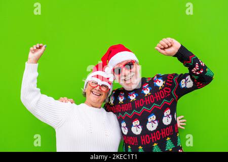 portrait de couple de deux aînés et des personnes âgées et matures ayant plaisir à profiter de noël ensemble portant des vêtements de noël et avec fond vert coloré Banque D'Images