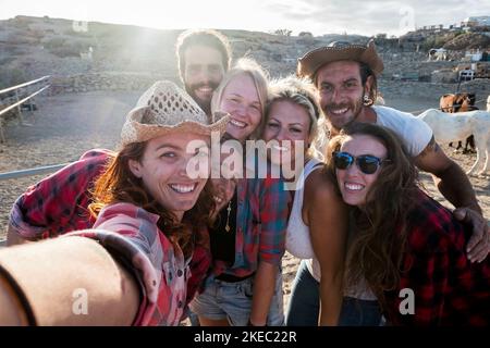 groupe de sept personnes s'amusant dans un ranch avec des chevaux - caucasiens qui prennent un selfie souriant et rire et plaisir Banque D'Images