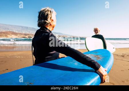 deux personnes âgées et matures appréciant leurs vacances à l'extérieur à la plage s'amuser avec des combinaisons et des planches de surf prêtes à aller surfer - senior actif faisant des sports nautiques à l'été Banque D'Images