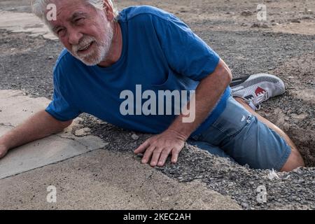 homme mature ou aîné marchant dans une zone de bâtiment et tomber dans un grand trou avec sa jambe à l'intérieur - besoin d'aide sur le terrain avec mal Banque D'Images