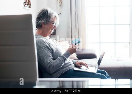 une femme mûre sur le canapé en utilisant son ordinateur portable et sa carte de crédit pour acheter quelque chose - shopping en ligne concept et shopaholic - senior à la maison faisant des cadeaux et présente avec les ventes Banque D'Images
