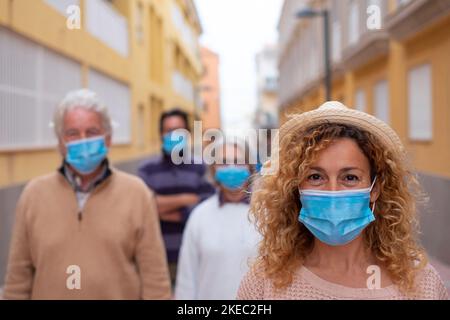 groupe de quatre personnes portant un masque médial et chirurgical et respectant la distance sociale dans la rue - adultes souriant et regardant la caméra dans le style de vie pandémique Banque D'Images