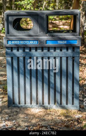 Une poubelle avec deux ouvertures l'une pour les déchets et l'autre pour les matières recyclables mélangées à l'entrée d'un sentier de randonnée dans la forêt, dans un parc au soleil Banque D'Images