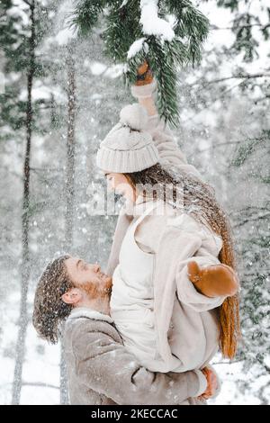 Romantique neige amour histoire.jeune couple gars fille couché, jouant dans la forêt d'hiver enneigée avec des arbres.Marche à pied, s'amuser, rire dans des vêtements chauds et élégants, Banque D'Images