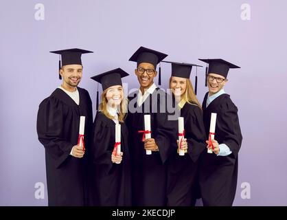 Portrait d'un groupe de diplômés heureux dans des mantes universitaires tenant des rouleaux de diplômes dans leurs mains. Banque D'Images