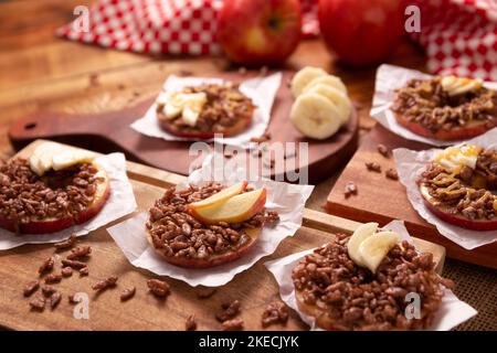 En-cas créatif pour les vacances. Ronds de pommes avec beurre d'arachide, garniture de riz soufflé au caramel et au chocolat et tranches de banane. Amuse-gueule Banque D'Images