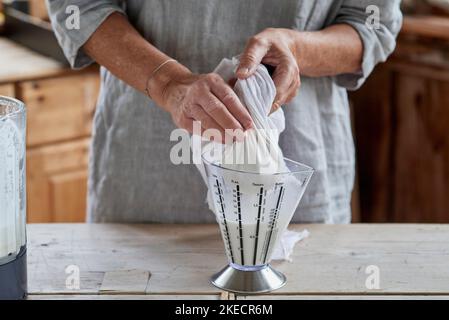 Étapes pour faire du lait d'amande, femme comprimant la masse écrasée dans la toile de gaze Banque D'Images