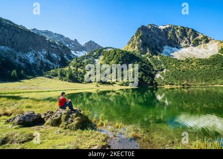 Randonneur assis au bord d'un lac de montagne idyllique entouré de montagnes enneigées le jour d'automne ensoleillé. Gaisalpsee avec Rubihorn, Alpes Allgäu, Bavière, Allemagne, Europe Banque D'Images