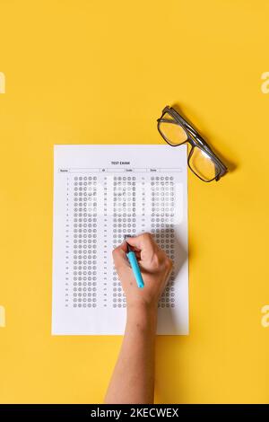 main d'une personne tenant un stylo et regardant une feuille de papier avec des chiffres sur elle sur un fond jaune Banque D'Images