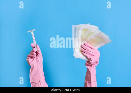 les mains de quelqu'un dans des gants en caoutchouc rose tenant une paire de ciseaux et de chiffons de nettoyage sur un fond bleu Banque D'Images