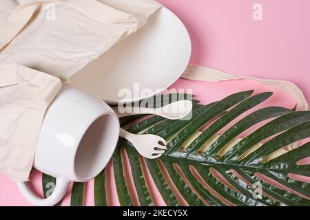 deux tasses blanches sur fond rose avec des feuilles de palmier dans la tasse se trouvent à côté de la tasse à café et de la cuillère Banque D'Images