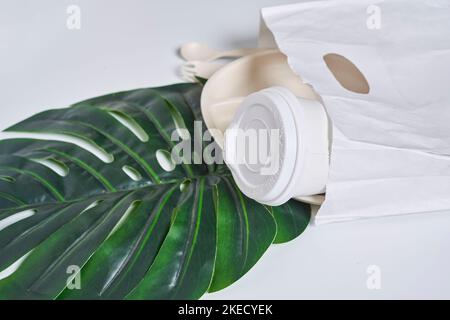 une tasse blanche et quelques feuilles vertes sur une surface blanche avec le café dans son sac de papier à côté Banque D'Images