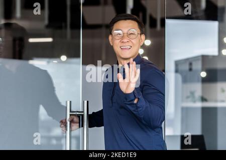 Premier jour de travail. Un jeune homme beau est venu à un nouvel emploi pour la première fois, entre dans le bureau, ouvre la porte, regarde dans la caméra, sourit, fait des vagues de sa main. Banque D'Images