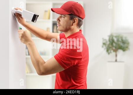 Photo de profil d'un jeune homme installant une caméra de sécurité sur un mur dans une pièce Banque D'Images