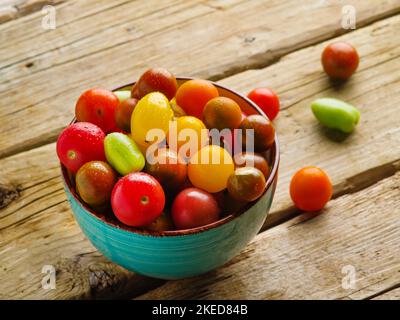 Sur une table en bois simple se trouve un bol de tomates fraîches colorées appétissantes. Gros plan. Nourriture biologique, mode de vie sain. Produit. Prêt à l'emploi. Il y a un Banque D'Images