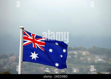Drapeau australien sur fond de maisons sur une colline et un ciel. Le drapeau australien est composé de six étoiles et du drapeau britannique. Banque D'Images