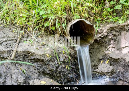 Eau s'écoulant de la sortie ouverte d'un carreau de drainage agricole métallique Banque D'Images