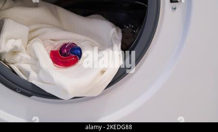 La capsule avec le gel de lavage se trouve dans le tambour de la machine à laver. Gel écologique de blanchisserie coloré en capsule. Clothers de lavage. Banque D'Images