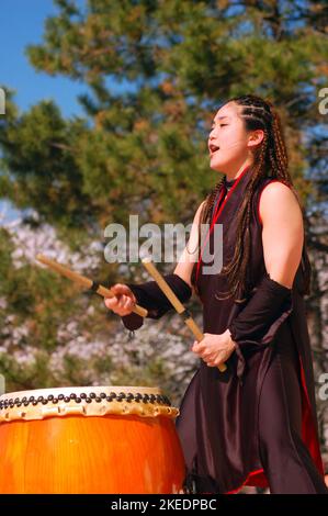 Une jeune japonaise montre les techniques de tambour de ttaiko anciennes et traditionnelles lors d'un festival de cerisiers en fleurs de sakura Banque D'Images