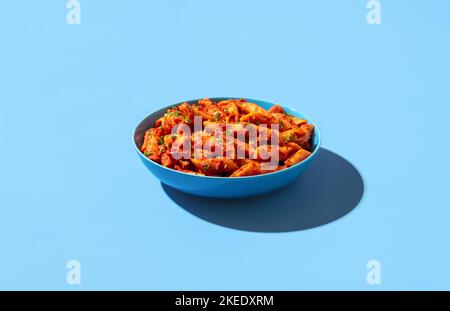 Penne alla arrabbiata bol minimaliste sur une table bleue. Délicieux plat italien, penne à la sauce tomate et flocons de piment. Banque D'Images