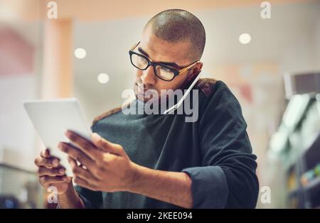 Un homme qui parle sur son téléphone portable dans un café tout en utilisant une tablette numérique, arrondit quelques détaillants en ligne. Banque D'Images