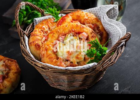 Mini pizza pour enfants, petites tartes ouvertes avec jambon, sauce tomate, mozzarella et fromage dans un panier sur fond sombre. Banque D'Images