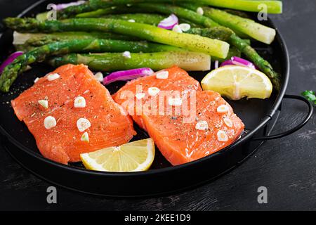Préparé pour cuire du saumon avec des asperges, des tranches de citron et des épices sur une table sombre. Banque D'Images