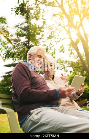 Garder leur retraite à jour. Un couple senior heureux utilisant une tablette numérique ensemble dans le parc. Banque D'Images