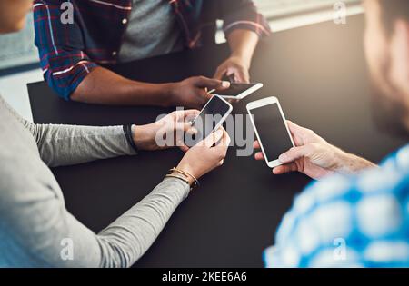 Tester la dernière application qu'ils ont créée ensemble. Trois personnes assises autour d'une table ensemble et utilisant leur téléphone portable. Banque D'Images