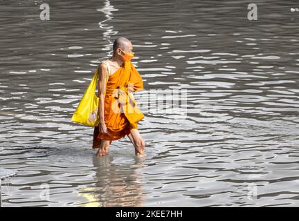 SAMUT PRAKAN, THAÏLANDE, OCT 29 2022, Un moine bouddhiste avec un sac marche dans l'eau dans une rue inondée Banque D'Images