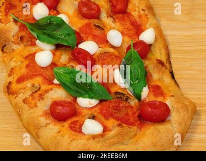 Pizza ou focaccia italienne cuite dans un four à bois avec tomates cerises et fromage mozzarella de buffle et basilic Banque D'Images