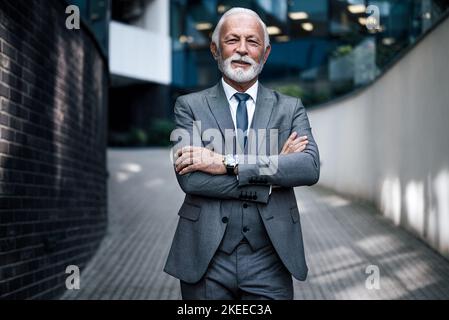 Homme âgé confiant professionnel avec les bras croisés. Portrait d'un homme d'affaires souriant se trouve sur une passerelle piétonne à l'extérieur du bureau Banque D'Images