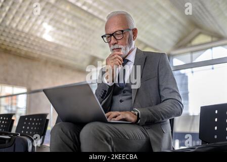 Homme d'affaires expérimenté et attentionné utilisant un ordinateur portable tout en étant assis sur une chaise. Un homme âgé de couleur professionnelle vous attend dans un métro ou un train de chemin de fer Banque D'Images