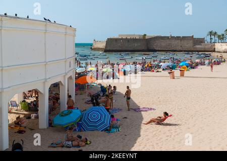 Cadix, Espagne: Baigneurs de soleil à Playa de la Caleta avec sur la gauche le Balneario de la Palma et en arrière-plan le Castillo de Santa Catalina. Banque D'Images