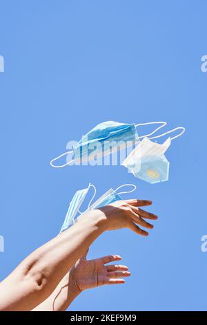 main de quelqu'un tenant une paire de masques chirurgicaux dans l'air contre un ciel bleu sans nuages Banque D'Images