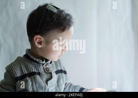 un petit garçon qui regarde quelque chose dans sa main pendant qu'il est assis sur la fenêtre et regarde vers le bas Banque D'Images