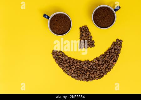 Émoticone souriant, lèvres en grains de café et yeux en tasses de café, composition sur fond jaune. Banque D'Images