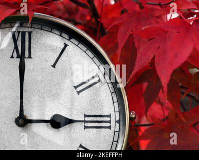 gros plan d'une ancienne horloge de la gare avec des chiffres romains montrant 3 heures devant les feuilles rouges d'automne, concept de changement d'heure en octobre Banque D'Images