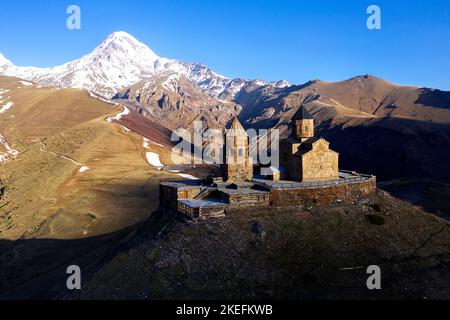 Vue aérienne de l'église de la Trinité de Gergeti au printemps lumière du matin avec montagne enneigée à l'arrière, Kazbegi, Géorgie, Europe Banque D'Images