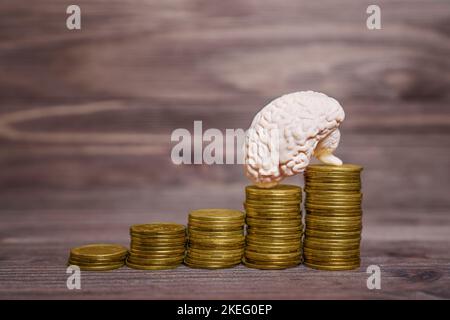 Copie anatomique d'un cerveau humain placé sur des piles de pièces de monnaie sur un fond en bois. Créativité investir dans votre concept d'esprit. Banque D'Images