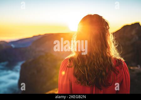 Description: Belle femme en robe rouge appréciant l'atmosphère de soirée ensoleillée sur Pico do Ariero. Verade do Pico Ruivo, île de Madère, Portugal, Europe. Banque D'Images