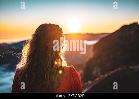 Description: Belle femme en robe rouge appréciant l'atmosphère de soirée ensoleillée sur Pico do Ariero. Verade do Pico Ruivo, île de Madère, Portugal, Europe. Banque D'Images