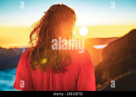 Description: Belle femme en robe rouge appréciant l'atmosphère de soirée ensoleillée sur Pico do Ariero. Verade do Pico Ruivo, île de Madère, Portugal, Europe. Banque D'Images