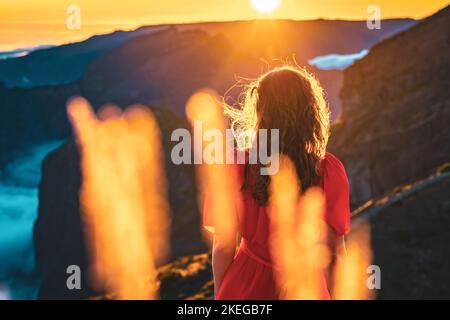 Description: Belle femme en robe rouge appréciant l'atmosphère de soirée ensoleillée sur Pico do Ariero. Verade do Pico Ruivo, île de Madère, Portugal, Europe. Banque D'Images