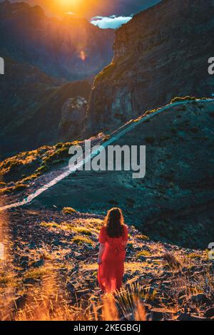 Description: Belle femme en robe rouge appréciant l'atmosphère de soirée ensoleillée sur Pico do Ariero. Verade do Pico Ruivo, île de Madère, Portugal, Europe. Banque D'Images