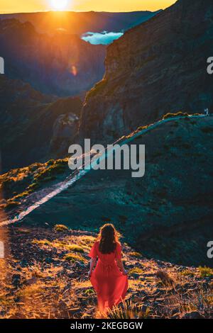 Description: Belle femme en robe rouge appréciant l'atmosphère de soirée ensoleillée sur Pico do Ariero. Verade do Pico Ruivo, île de Madère, Portugal, Europe. Banque D'Images