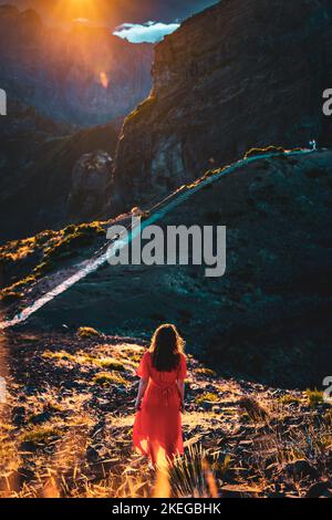 Description: Belle femme en robe rouge appréciant l'atmosphère de soirée ensoleillée sur Pico do Ariero. Verade do Pico Ruivo, île de Madère, Portugal, Europe. Banque D'Images