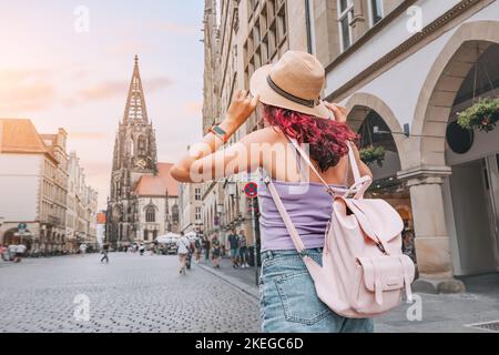 Une heureuse femme touristique avec sac à dos visitant la rue Prinzipalmarkt et admirant les bâtiments de l'architecture de la vieille ville à Munster, en Allemagne Banque D'Images