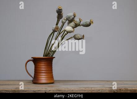 têtes de graines de pavot séchées dans un vase en céramique sur une table en bois Banque D'Images